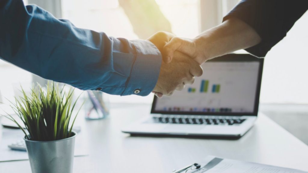 Two individuals shaking hands over a laptop, symbolizing a partnership for Palmetto SEO.