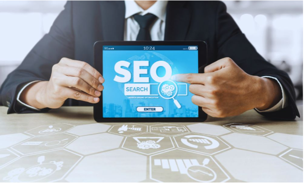 A business professional in a suit sits at a desk, holding a tablet that displays the words “SEO SEARCH” with a magnifying glass icon. The modern office background includes digital marketing icons, reflecting themes related to search engine optimization services in Kendall.