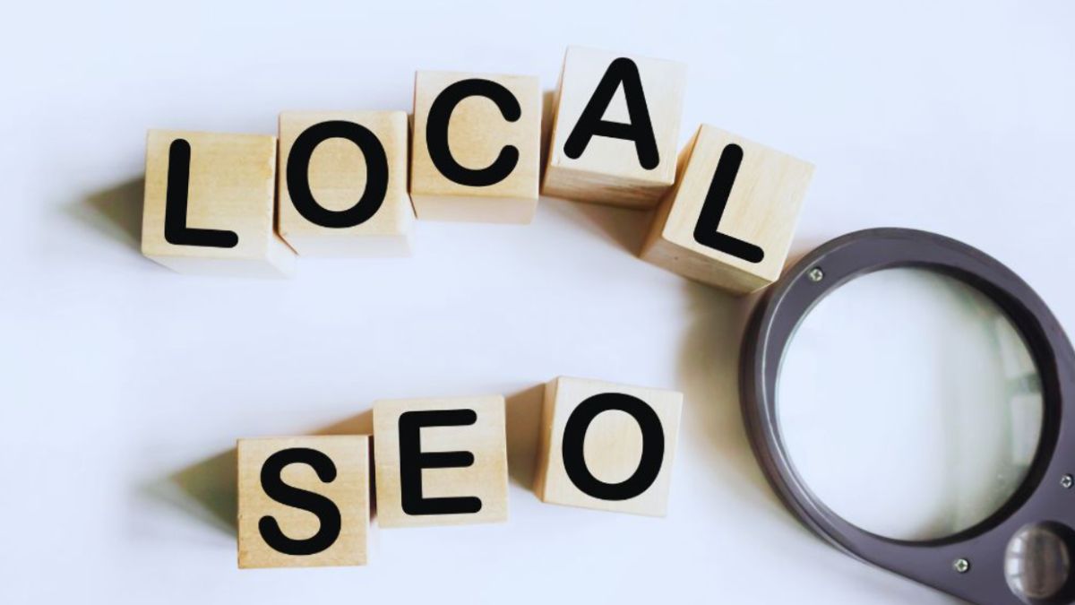 Wooden blocks arranged to spell out LOCAL SEO in black letters on a white background, with a gray magnifying glass placed beside them.