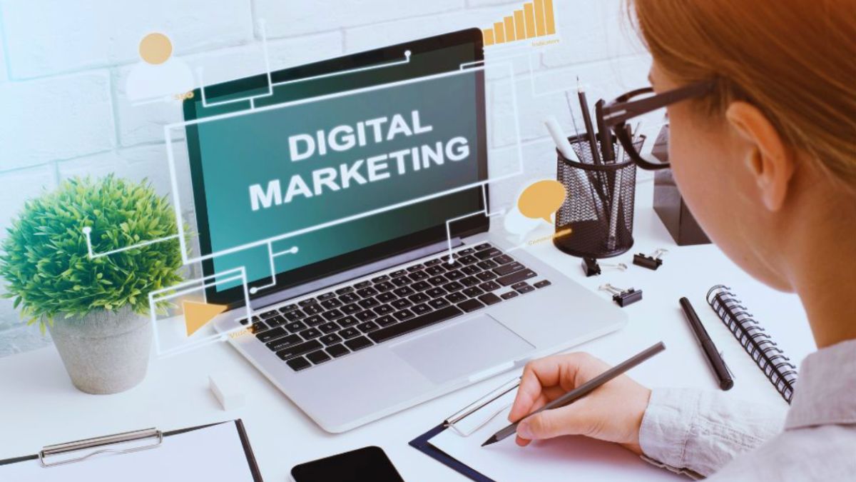Hands on a laptop showing “DIGITAL MARKETING” on screen at a tidy desk.