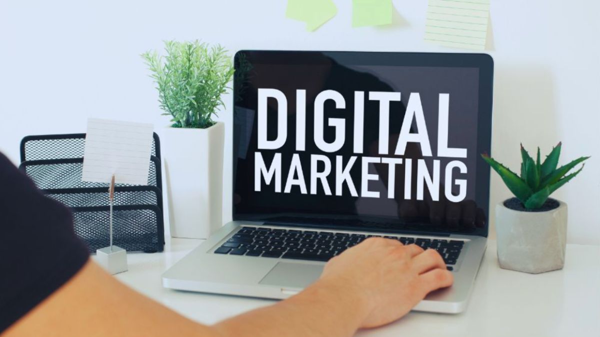 A person working on a laptop displaying the words “DIGITAL MARKETING” on the screen, with small plants and office supplies on a clean white desk, representing a modern professional online marketing agency workspace.